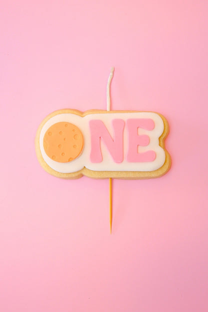 Candle shaped like the number 'ONE' on a pink background with orange planet 