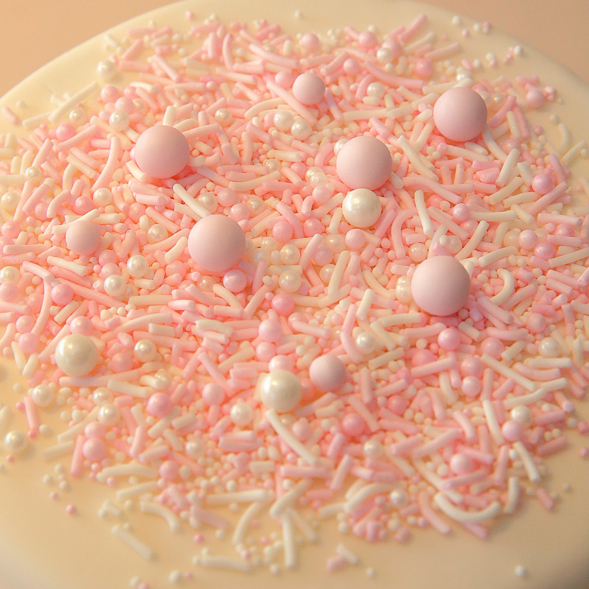 Close-up of a cake covered in pink and white sprinkles on a beige background