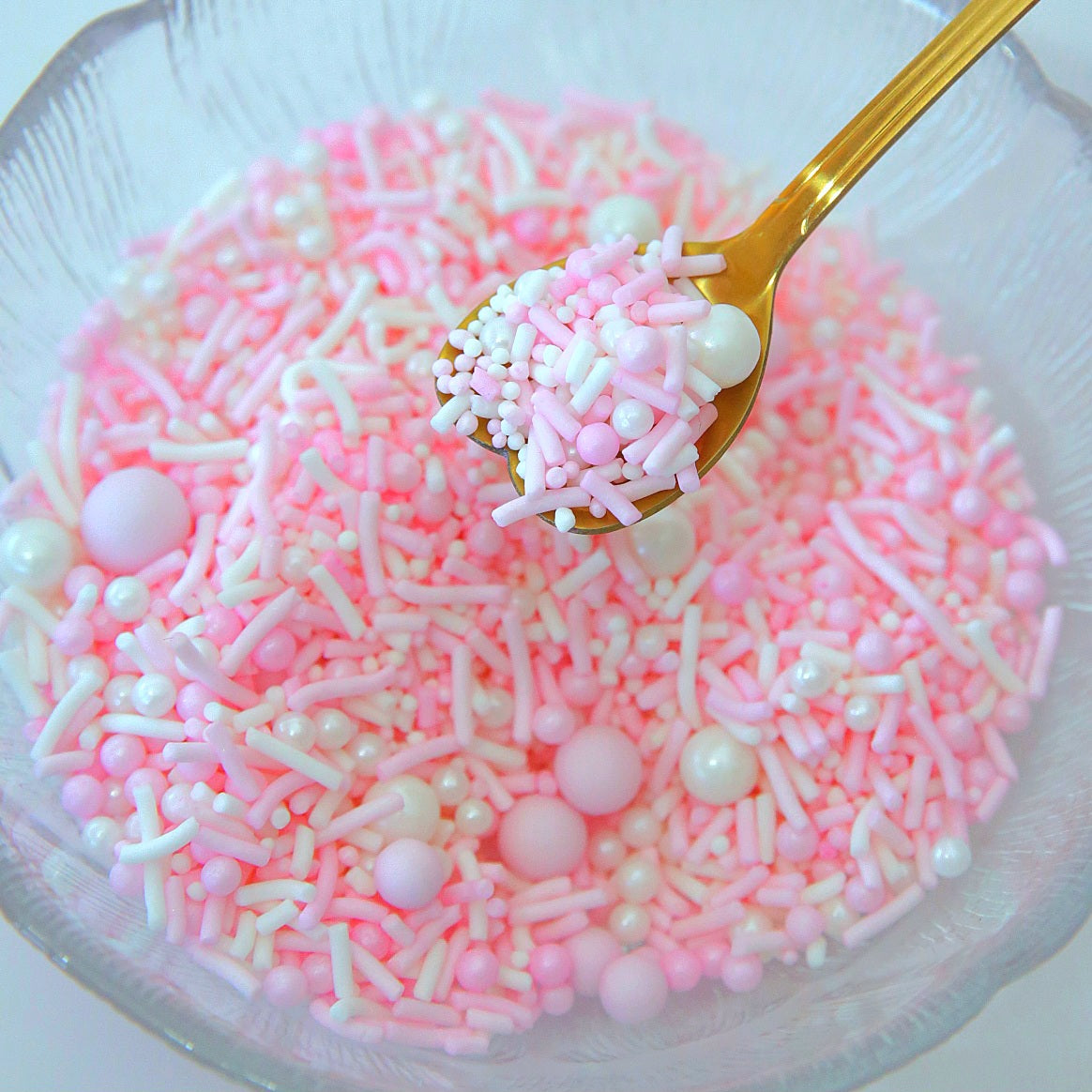 Glass bowl filled with pink and white sprinkles with a gold spoon.