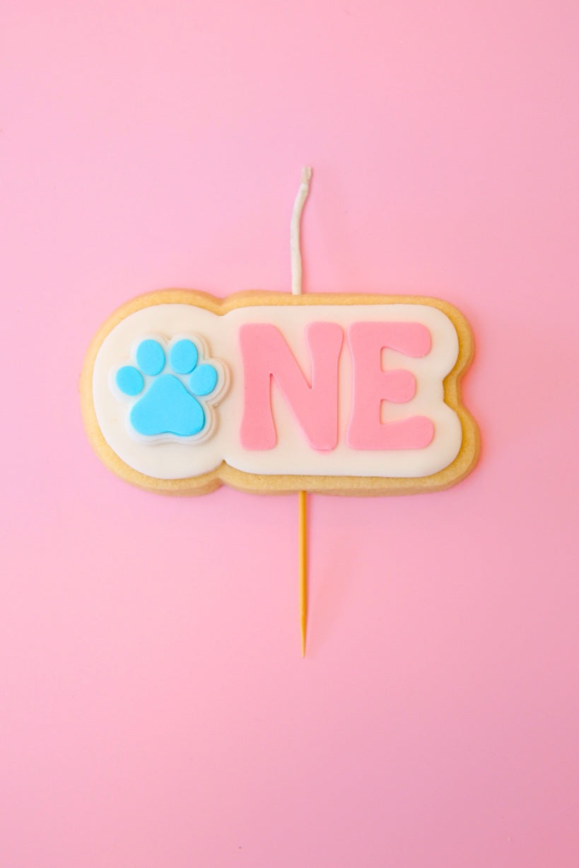 Candle shaped like the number 'ONE' with a paw print on a pink background