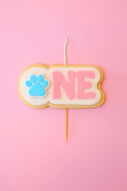 Candle shaped like the number 'ONE' with a paw print on a pink background