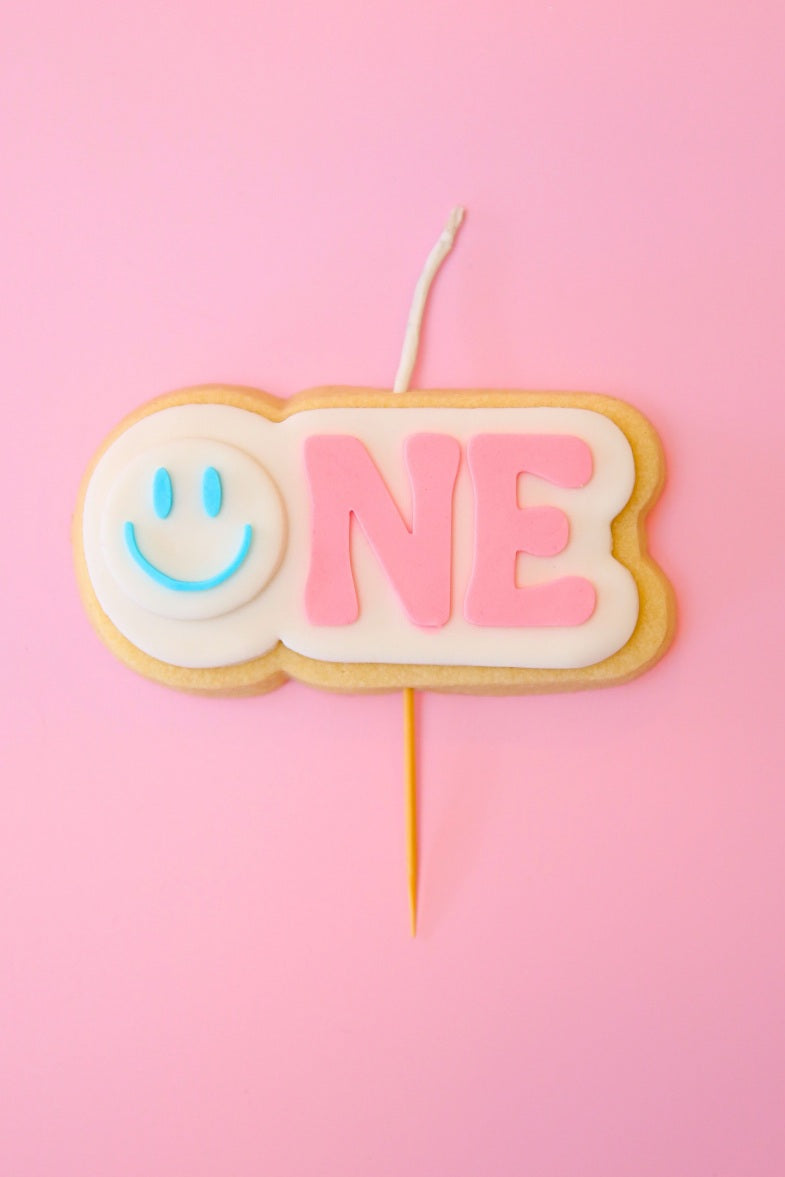 Candle shaped like the number '1' with a blue smiley face on a pink background