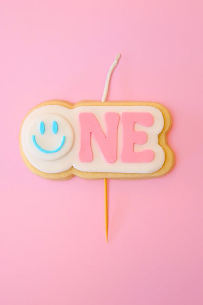 Candle shaped like the number '1' with a blue smiley face on a pink background
