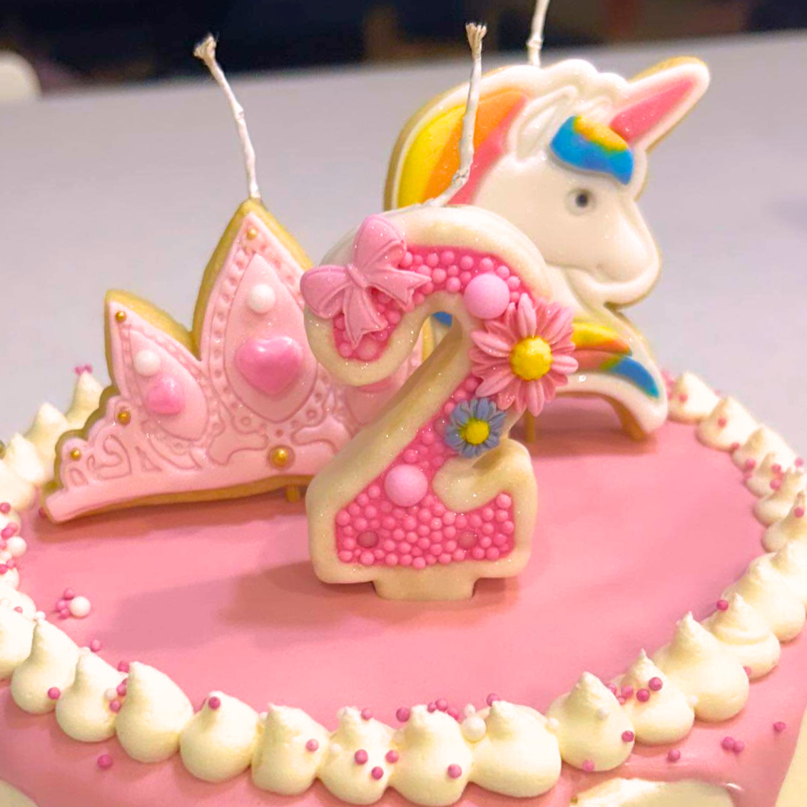 Pink birthday cake with unicorn, tiara and number 2 cookie candle decorations