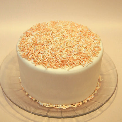 White cake with orange and white sprinkles on a clear glass plate.