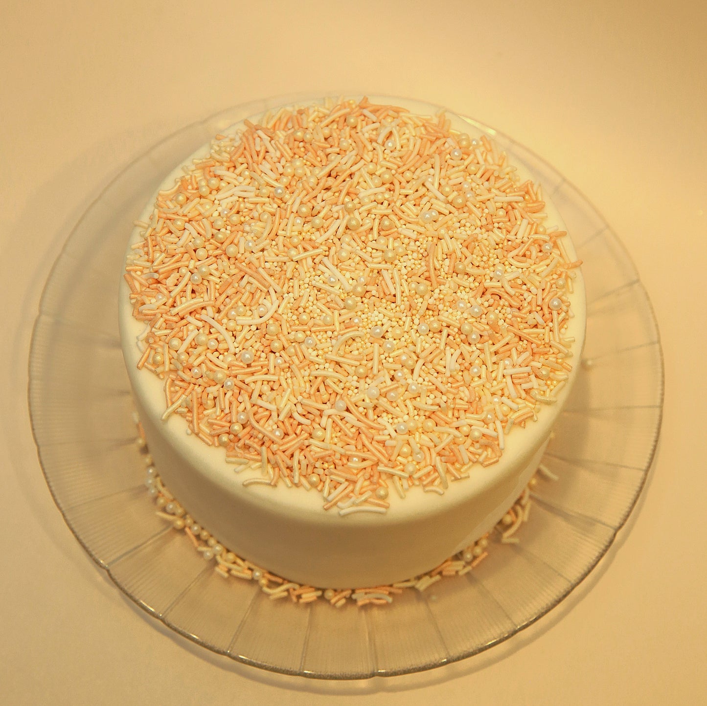 Cake with orange and white sprinkles on a clear plate against a beige background