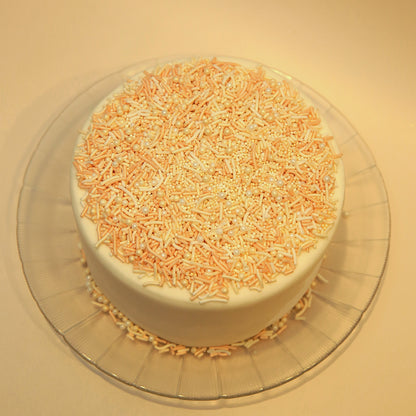 Cake with orange and white sprinkles on a clear plate against a beige background